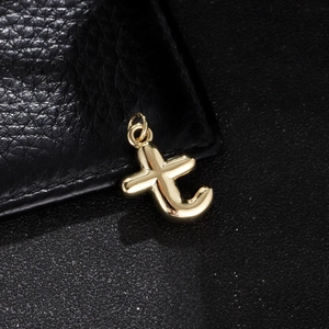 Macro detail of polished gold-plated lowercase t-letter charm on a dark leather surface