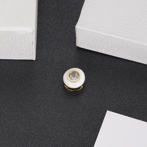 Macro shot of white enamel bead featuring a central clear zircon set in gold metal