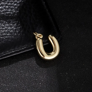 Close-up of a polished gold letter U bubble pendant on a black textured background
