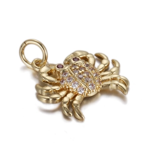 Detailed view of a gold crab charm inlaid with pink cubic zirconia and red gem eyes