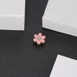 Close-up of pink flower jewelry charm with gold edges and CZ stones on a black surface