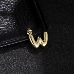 Macro shot of gold bubble letter W pendant with a polished mirror finish on black leather