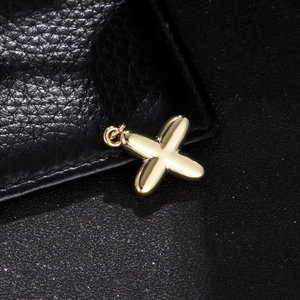 Macro shot of a golden polished balloon X-shaped pendant on black leather background