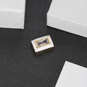 Macro detail of a gold plated rectangle pendant with white enamel and clear zircon