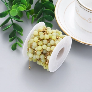 Detailed view of light green stone beads with golden metal spacers on a white spool