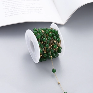 Detail of dark green natural stone beads and gold chain on spool for DIY jewelry making