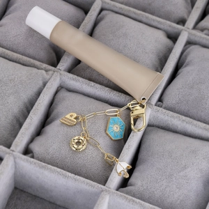 Tubo de bálsamo labial con cadena dorada y colgantes de corazón sobre fondo de terciopelo