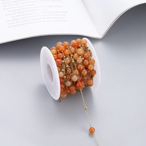 Detail of orange translucent beads on a gold chain wound around a white plastic spool