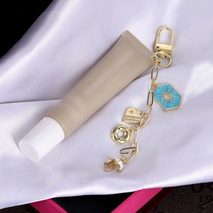 Llavero dorado con colgantes de sol azul y corazón unido a un tubo de cosméticos