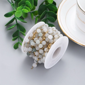 Detailed close-up of handmade jewelry chain with grey beads on white plastic spool