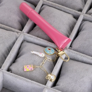 Detalle de un tubo cosmético rosa con dijes de esmalte y un llavero dorado elegante