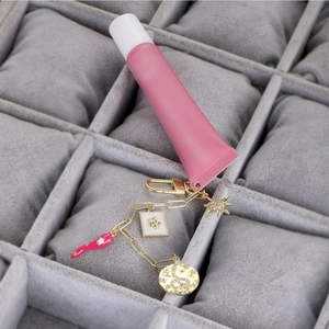 Detalle de un llavero dorado con brillo de labios rosa y dijes de esmalte