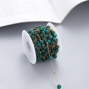 Close-up of DIY gold chain with dark green stone beads wound on a white spool
