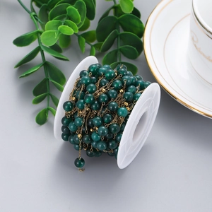 Detailed view of dark green stone bead chain with gold links on a white spool for DIY jewelry