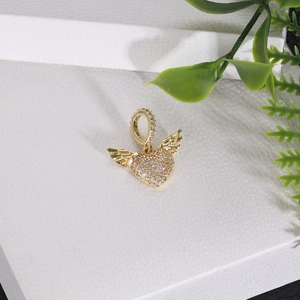 Detailed close-up of a gold heart pendant with crystal wings on white texture