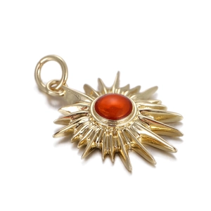Macro detail of sunburst charm with central red stone and gold plating finish