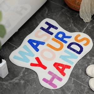 Irregular plush bath mat with colorful Wash Your Hands text on grey marble floor