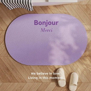 Purple oval absorbent bath mat with Bonjour print on wood floor with tree shadows
