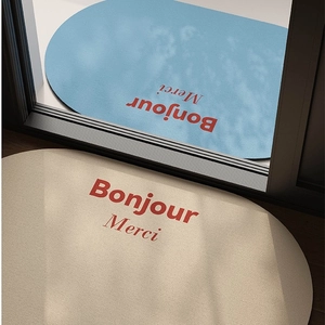 Absorbent non-slip oval bath mat with Bonjour and Merci text on a wooden floor