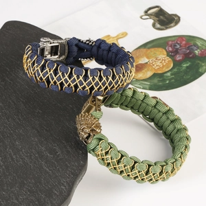 Detail of paracord woven bracelets featuring skull and lion brass charms on rock surface