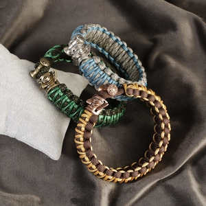 Three tactical braided parachute cord bracelets with vintage mask metal charms on grey fabric