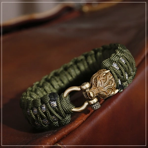 Makroaufnahme von grünem Paracord-Armband mit bronzenem Wolfskopf-Metallverschluss