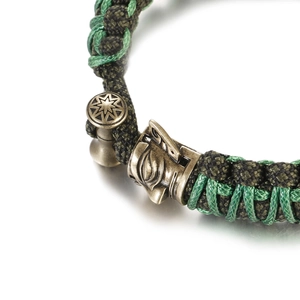 Macro shot of green braided paracord bracelet with antique bronze star emblem and mask charm