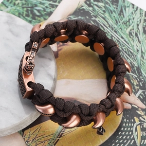 Detail eines Paracord-Webarmbands mit Vintage-Wolfszahn-Metallanhängern in Kupfer