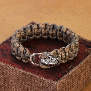 Detail of paracord bracelet with silver skull charm and metal U-shackle on jewelry box