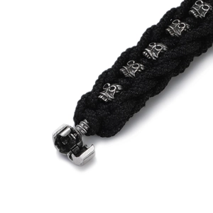 Detail view of black braided men's bracelet with vintage skull charms and screw clasp