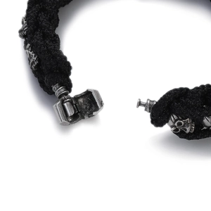 Close-up of black braided chain bracelet with silver skull charm and mechanical clasp