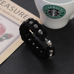 Close-up of black braided cord bracelet with silver skull charms and a metal clasp