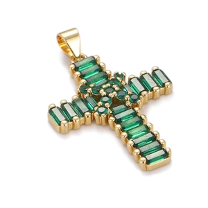Macro shot of gold cross pendant with rectangular and round cut green gemstones