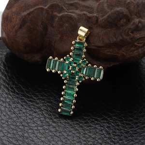 Macro detail of gold-plated cross pendant with inlaid green emerald-like gemstones