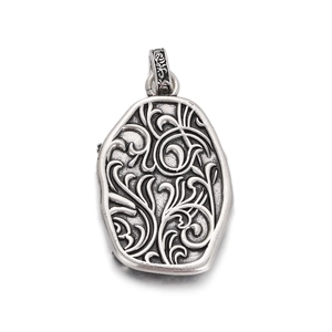 Close-up of vintage silver pendant featuring intricate engraved vine patterns and antique finish