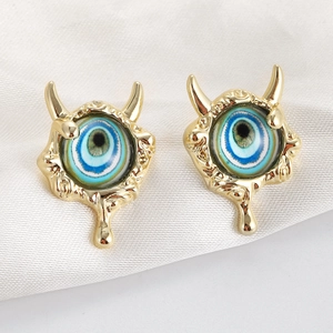 Macro shot of evil eye studs with golden molten metal drip design and blue eyeball