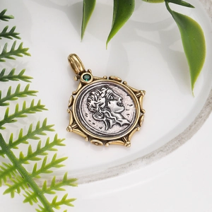 Detail of vintage bronze coin pendant with emerald green stone on white ceramic plate