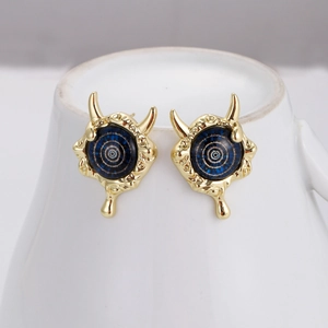 Macro detail of gold devil eye stud earrings with blue enamel and horn design