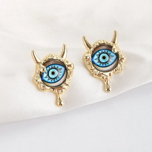 Macro detail of golden devil eye stud earrings with blue core on white satin fabric