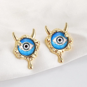 Macro detail of blue evil eye earrings with golden devil horns and molten metal texture