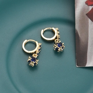 Detailed macro view of 18K gold hoop earrings with deep blue zircons on green surface