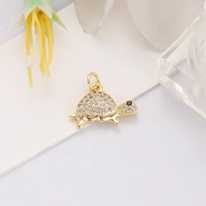 Detailed view of a gold turtle pendant with white zircon shell and black gemstone eye