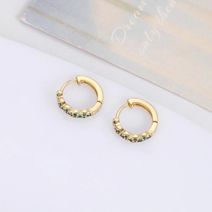 Close-up of gold-plated huggie hoop earrings with green zircon stones on white background