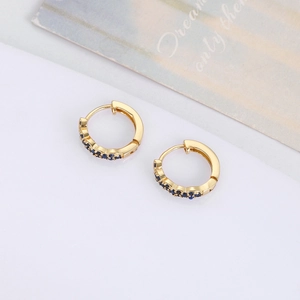 Macro shot of gold-plated huggie hoop earrings with navy blue zircon stones and wavy edge
