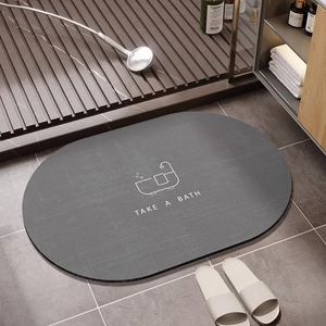 Dark grey oval diatomite bath mat with Take A Bath text in a modern bathroom setting
