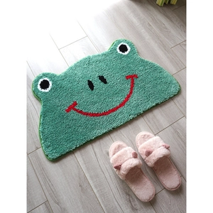 Close-up of green cartoon frog bath mat with plush texture on grey wooden floor