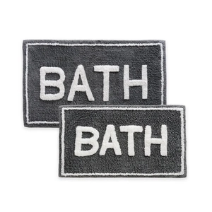 Detailed view of two dark grey faux cashmere bath mats featuring white BATH lettering
