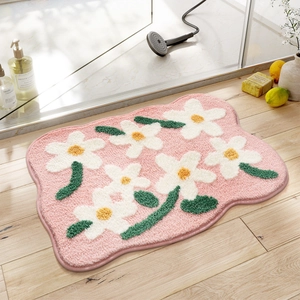 Detailed view of pink floral tufted bathroom mat with white daisy pattern on wood floor