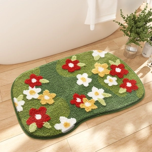 Detail of green floral bath mat with 3D tufted red and yellow flowers on wood floor