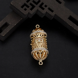Macro view of gold plated cylindrical pendant with evil eye motif and white zircons